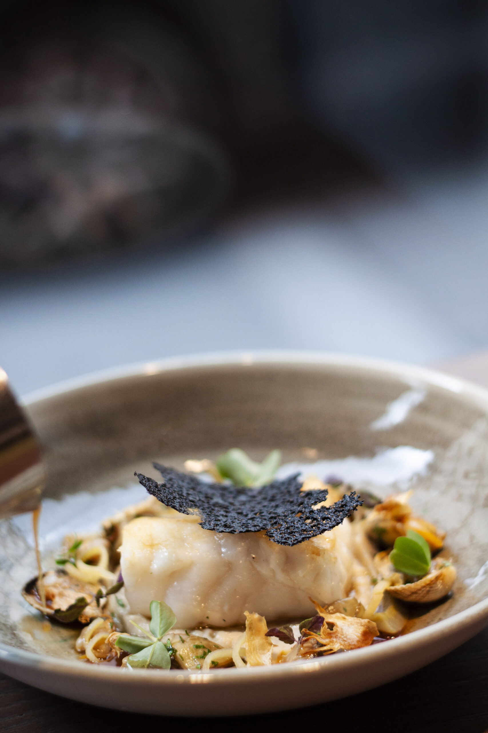 Plat culinaire artisanal réalisé par un artisan chef, composé d’un poisson délicatement dressé avec légumes, herbes fraîches et tuile croustillante, servi dans une assiette élégante