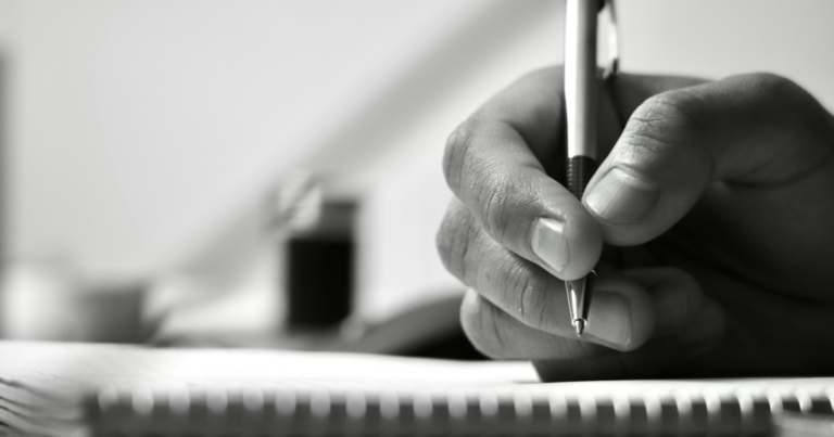 Main tenant un stylo au-dessus d'un carnet ouvert - Unsplash