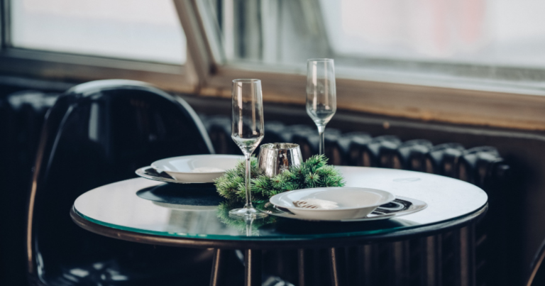 Table dressée pour un dîner, verres à pied et bougie, lumière du soir devant une fenêtre - Unsplash